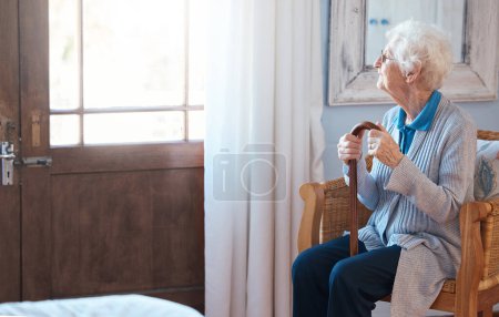 Foto de Mujer pensante, triste y mayor pensando en la vida con un bastón junto a la ventana en la habitación de una casa de retiro. Mujer anciana con depresión, discapacidad e idea de jubilación en un hogar de ancianos. - Imagen libre de derechos