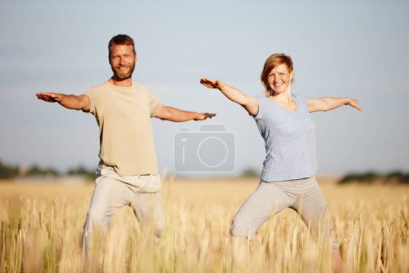 Téléchargez les photos : Le yoga fait partie de leur style de vie. un couple mature en position guerrière lors d'un entraînement de yoga dans un champ - en image libre de droit