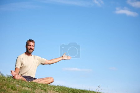 Showing you the way to wellness. Portrait of a handsome mature man presenting copyspace while sitting in the lotus position outdoors