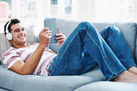 Its the perfect way to relax. An attractive man lying on the sofa at home and listening to music on his tablet