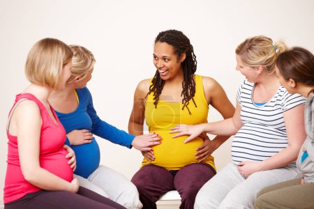 Foto de Sentí una patada. Un grupo de amigas embarazadas tocando el vientre de sus amigas afroamericanas mientras sonríen - Imagen libre de derechos