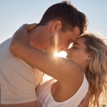 Love, beach hug and couple face together on sunset vacation date by the sea for romance, affection and relationship commitment. Happy man, woman with a smile and romantic ocean summer holiday getaway.