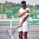 Sports, tennis and arm pain on court after training, game or match outdoors. Healthcare, tennis player and injured black man or athlete with muscle pain or inflammation after exercise or workout
