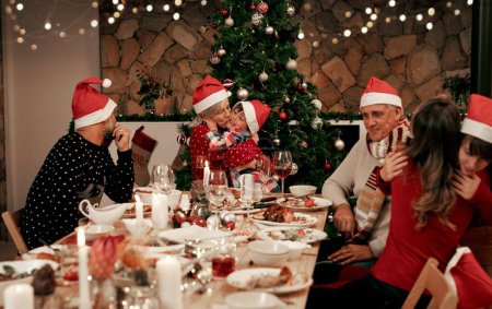 Familie, Generationen und Weihnachtsfeier mit Männern, Frauen und Kindern lächeln, essen und trinken gemeinsam im Speisesaal. Glückliche Familie, Kinder, Paar und Großeltern feiern festliche Umarmung am Tisch