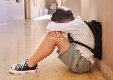 Anxiety, school and sad student bullying victim feeling depression, lost or stressed in hallway or corridor floor. Child, depressed boy or lonely male learner crying alone with abuse trauma or fear.