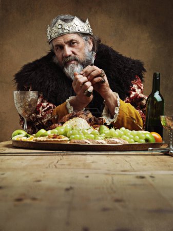 Foto de Ser rey tiene sus ventajas. Un rey maduro festejando solo en una sala de banquetes - Imagen libre de derechos
