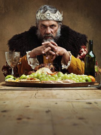 Foto de Se divierte mientras los siervos mueren de hambre. Un rey maduro festejando solo en una sala de banquetes - Imagen libre de derechos