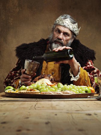 Foto de Creo que voy a necesitar más vino. Un rey maduro festejando solo en una sala de banquetes - Imagen libre de derechos