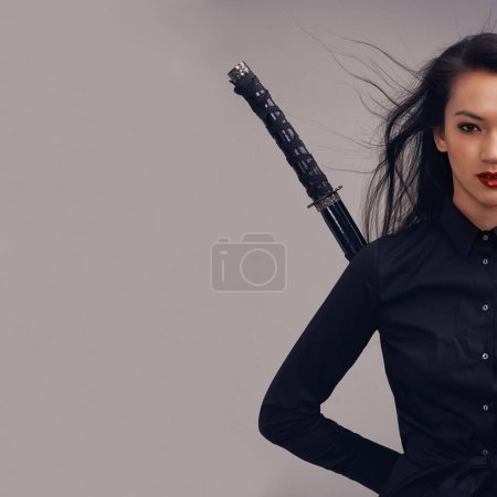 Ihr Schwert ist eines, das schützt. Ausgeschnittenes Studioporträt einer schönen jungen Frau im Kampfsport-Outfit, die ein Samurai-Schwert schwingt