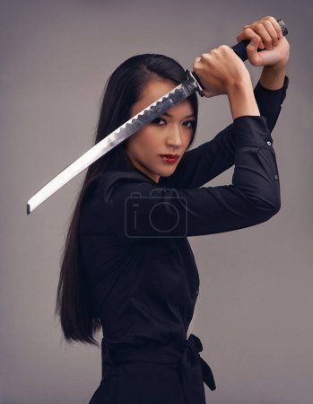 Der Weg des Samurai. Studioporträt einer schönen jungen Frau im Kampfsport-Outfit, die ein Samurai-Schwert schwingt