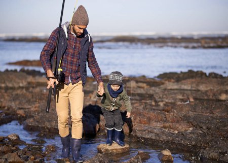 Téléchargez les photos : Nous y allons... un père et son fils marchant sur les rochers tout en pêchant ensemble par la mer - en image libre de droit