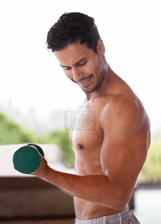 Photo for Checking out his guns. a handsome man lifting dumbbells at home - Royalty Free Image