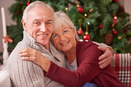 Foto de Navidad, amor y retrato de una pareja mayor abrazándose, uniéndose y relajándose en un sofá juntos. Feliz, sonrisa y anciano hombre y mujer en retiro celebrando Navidad en una fiesta festiva en casa - Imagen libre de derechos