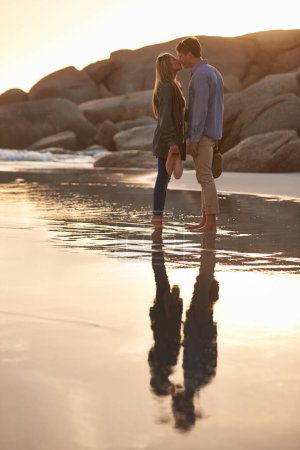 Photo pour Amoureux enfermés dans un moment d'amour. un jeune couple profitant d'un baiser romantique sur la plage au coucher du soleil - image libre de droit