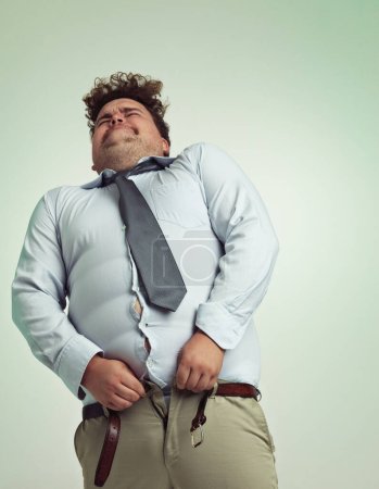 Photo for Almost closed...Humorous studio shot of an overweight businessman trying to button his pants - Royalty Free Image