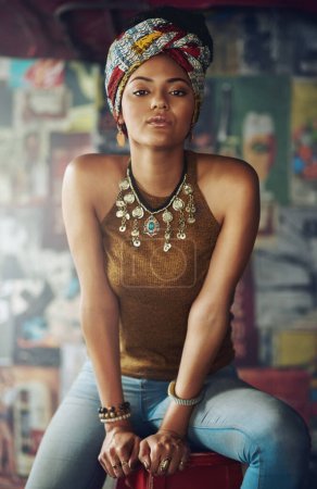 Portrait, fashion and heritage with a black woman on a stool indoors with an African style turban. Model, culture and tradition with an attractive young female feeling empowerment or proud.