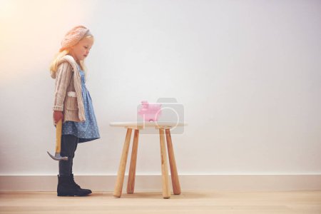 Photo for Learning about the importance of saving. A little girl standing next to her piggy bank with a hammer - Royalty Free Image