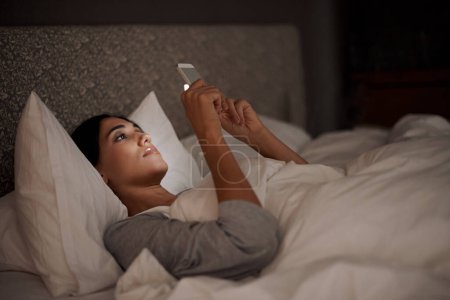 Photo for Saying goodnight to my love. A young woman sending a text message while in bed - Royalty Free Image