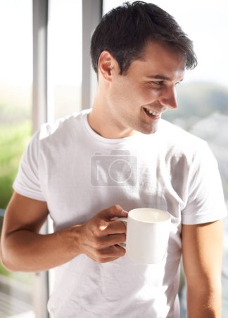 Ich genieße meine Aussicht mit einer frischen Tasse Kaffee. ein hübscher junger Mann trinkt Kaffee, während er am Schlafzimmerfenster steht