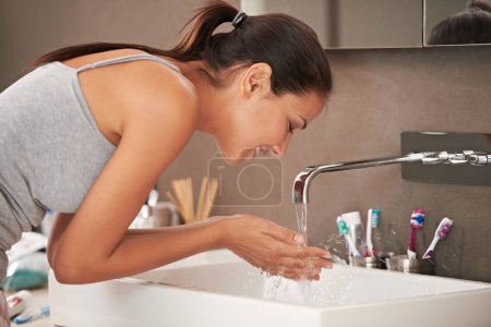 Photo for Cleanliness is next to godliness. A beautiful young woman washing her face in her bathroom - Royalty Free Image
