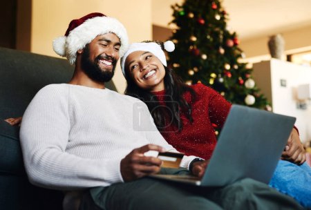 Weihnachten, Paar und Couch mit Laptop, Kreditkarte und zusammen für Finanzen, Festtage und E-Commerce in Lounge. Xmas, Mann und Frau für Zahlungen, Investitionen und Online-Banking für Transaktionen.