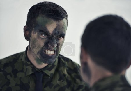 Photo for Ready for war. A military man with his face camouflaged making a mean face while looking in the mirror - Royalty Free Image