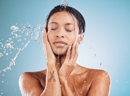 Water, cleaning and shower with a black woman in studio on a blue background for hygiene or hydration. Relax, skincare and wellness with an attractive young female washing her skin in the bathroom.