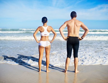 Lets do this. A man and woman standing with their hands on their hips in front of the sea