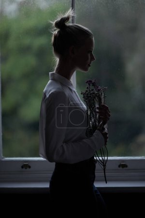 Photo for Let your imagination take flight. A young woman standing by a window holding flowers - Royalty Free Image