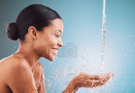 Photo for Skincare, health and black woman with water splash, wellness and hygiene against a blue studio background. Cosmetics, young female and girl with smile, drops and natural beauty for washing and relax - Royalty Free Image