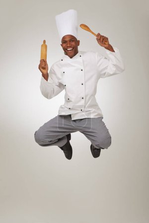 Foto de Este chef es un gran apostador. Un chef afroamericano saltando en el aire sosteniendo un rodillo y una cuchara - Imagen libre de derechos