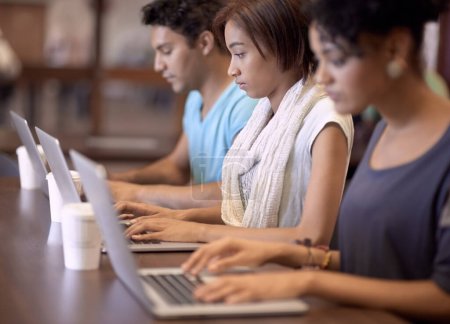 Foto de Estos estudiantes están trabajando duro. Un grupo de estudiantes que utilizan una computadora portátil para completar una asignación de grupo - Imagen libre de derechos