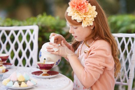 Téléchargez les photos : Organiser un goûter. Une mignonne petite fille ayant une partie de thé dehors - en image libre de droit