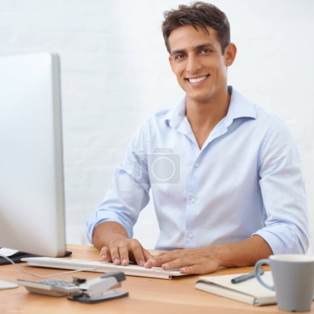 Téléchargez les photos : Intégrer l'esprit d'entreprise. Un jeune homme d'affaires heureux assis derrière son bureau et souriant avec confiance à la caméra - en image libre de droit