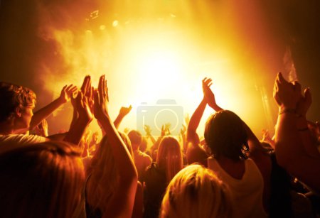 Music, concert and crowd with light, clapping for live performance, rock event and band on stage at night. People, audience and music festival, audio and sound with energy at show with musical artist.