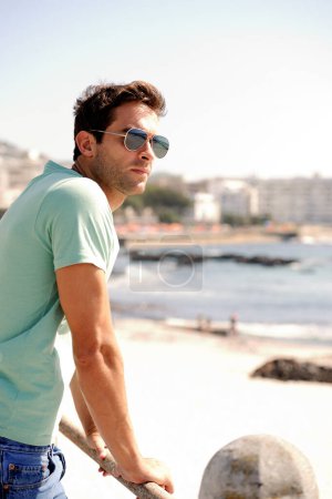 Foto de Tomando tiempo para aclarar su mente. Un joven guapo con gafas de sol y admirando la vista en primera línea de playa - Imagen libre de derechos