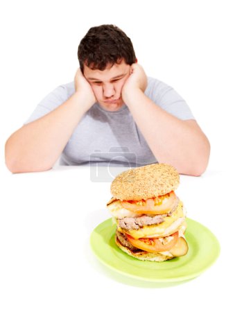 Photo for That looks like another 5 pounds. A dejecting young obese man holds his head in his hands while looking at a huge burger - Royalty Free Image