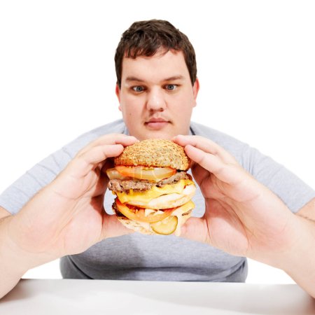 Photo for Hello burger Youre about to be eaten. A young obese man looking yearningly at the burger he is holding - Royalty Free Image