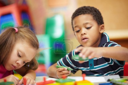 Photo for Learning and developing. Pre-school ethnic boy and girl scribbling and drawing with multi-coloured crayons in pre-school classroom - Royalty Free Image