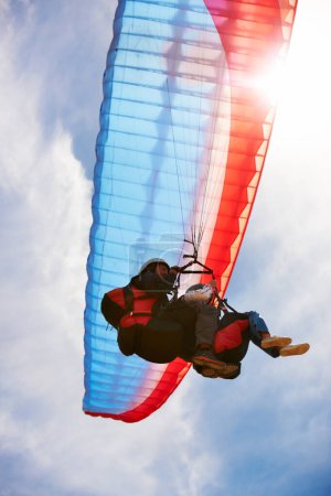 Photo for Up and away. View from directly below two people doing tandem paragliding with the sun and sky in the background - Royalty Free Image