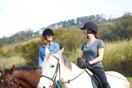 Foto de Disfrutando montando sus caballos en los campos abiertos. Dos mujeres jóvenes hablando mientras cabalgan - Imagen libre de derechos