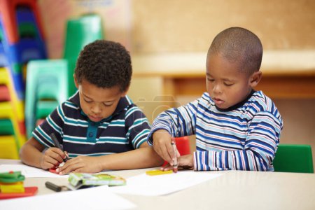 Photo for Working together on their creativity. Two preschool african american boys concentrating on thier drawings with thier crayons and shapes - Royalty Free Image