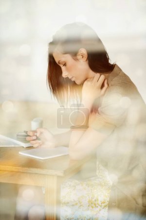 Jotting down her thoughts...Attractive young woman writing in her diary while in a coffee shop