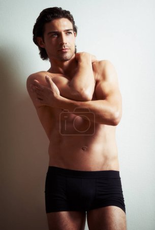 Photo for Lingering gaze. A sexy semi-nude young man leaning against a wall - Royalty Free Image
