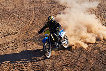 Photo for Leaving his competitors in the dust. A dirt biker riding along a track with a cloud of dust following him - Royalty Free Image