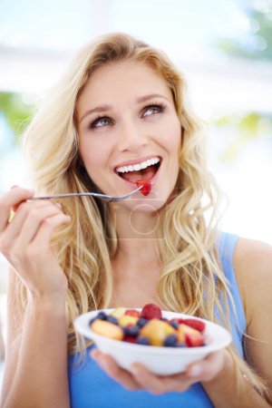 Foto de Anticipándose a un delicioso sabor. Mujer joven y bonita mirando hacia arriba mientras come su ensalada de frutas - Imagen libre de derechos