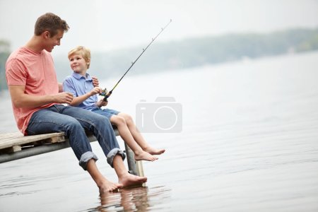 Téléchargez les photos : Qualité Père et fils temps. Un père apprenant à son fils à pêcher assis sur un rebord au-dessus d'une rivière - en image libre de droit