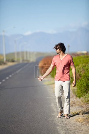 Photo for I guess Ill have to hitchhike. A young man trying to hitch a ride while walking along a deserted road - Royalty Free Image