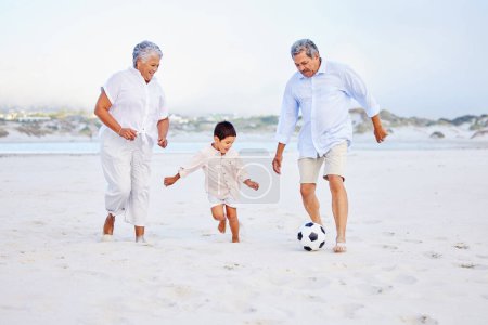 Photo for Active grandparents playing soccer on the beach with their grandson. Little boy kicking ball with his grandmother and grandfather on shore. - Royalty Free Image