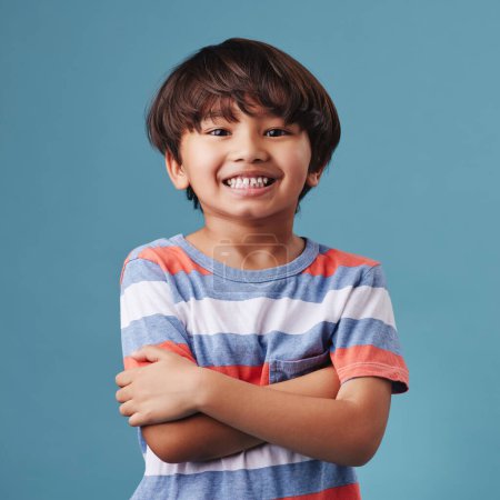 Téléchargez les photos : Portrait d'un petit garçon asiatique mignon portant des vêtements décontractés tout en souriant et en regardant excité. Enfant debout sur un fond bleu studio. Adorable petit garçon heureux en sécurité et seul. - en image libre de droit